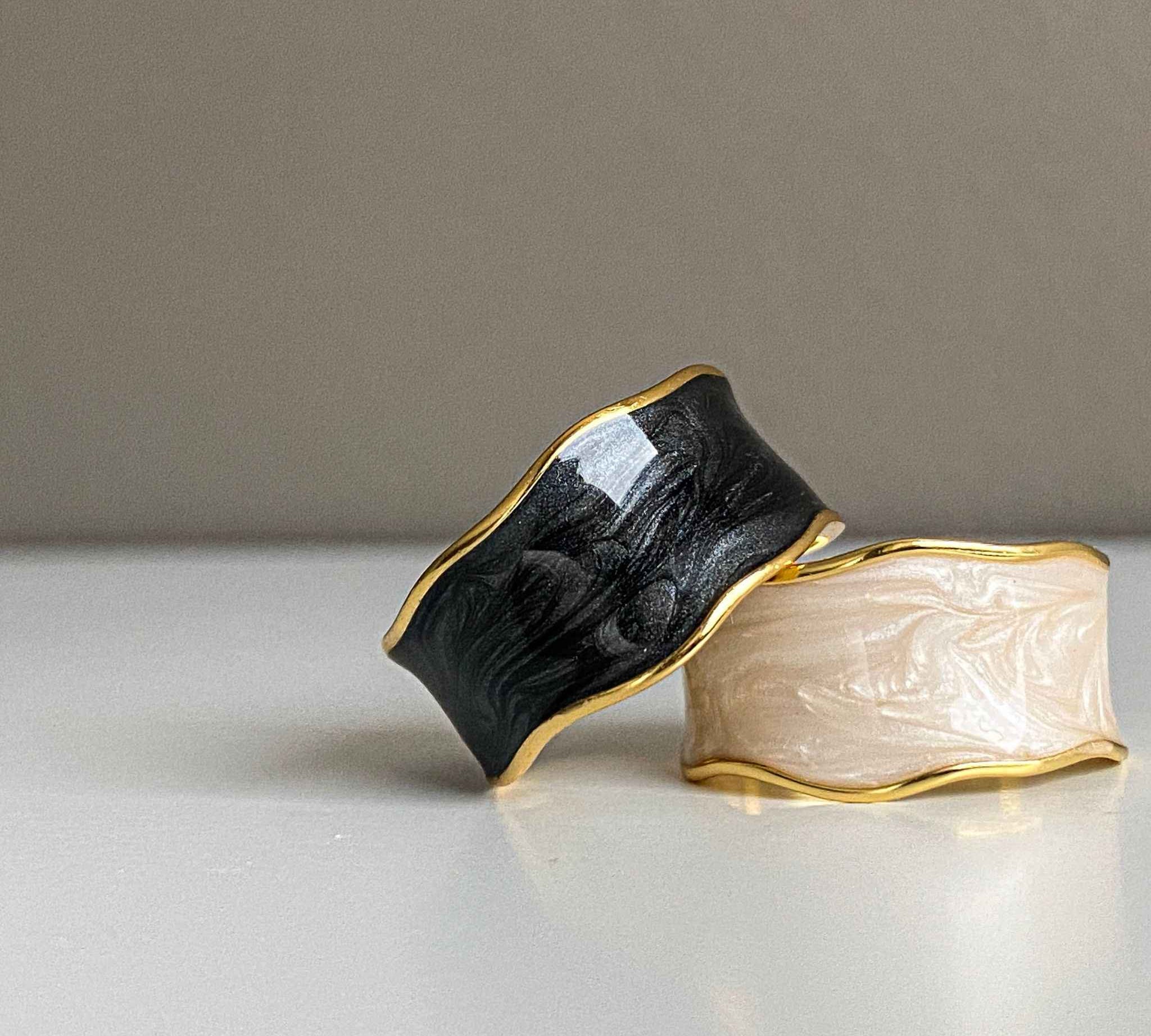Close-up view of the white enamel swirl design on the gold plated ring, along with the same ring in black.