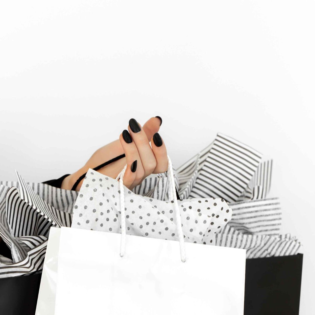 A woman's hand with black painted fingernails, holding a variety of white and black shopping bags.