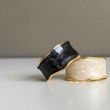 Close-up view of the white enamel swirl design on the gold plated ring, along with the same ring in black.