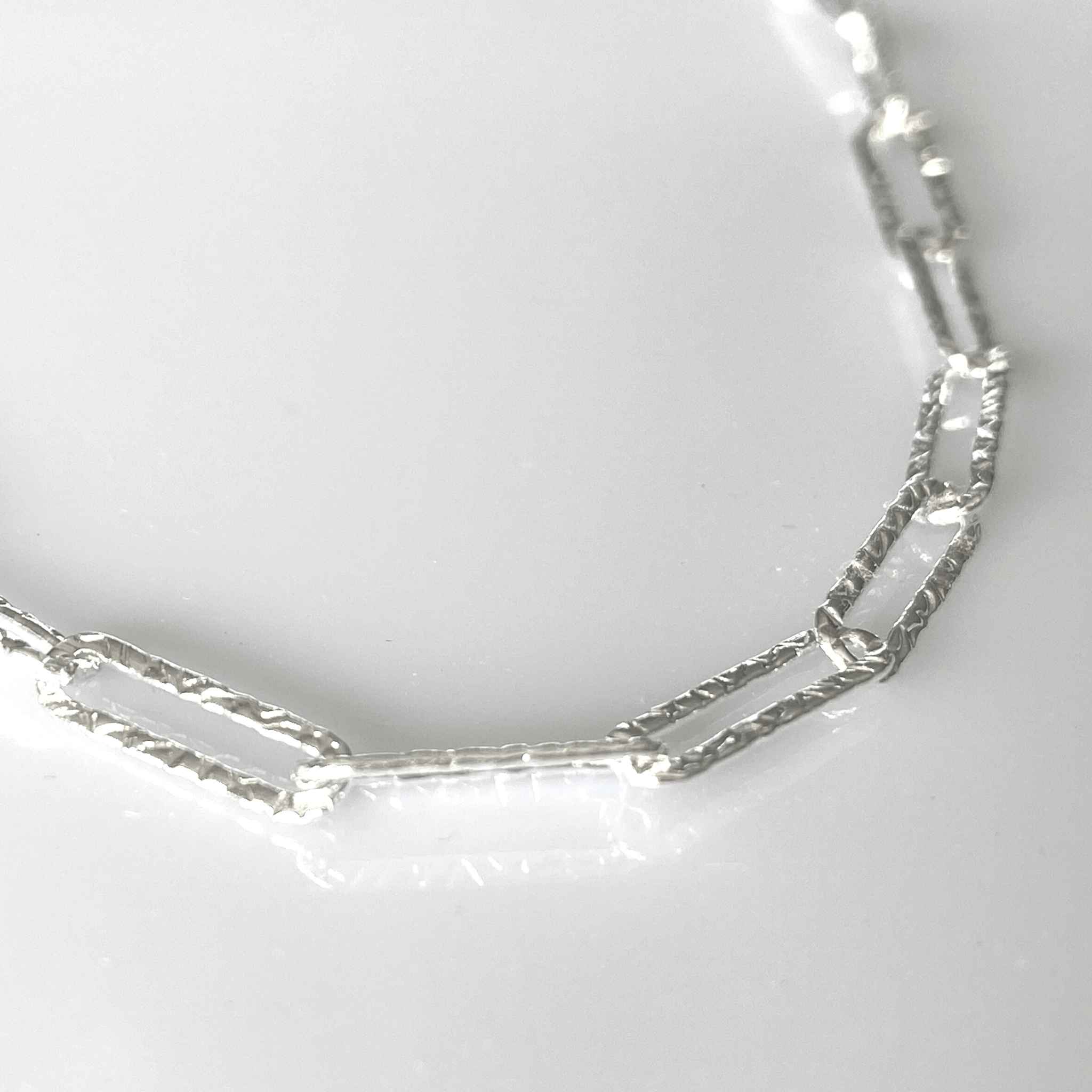 Close-up of the hammered links of the silver paperclip chain necklace, reflecting detailed craftmanship.