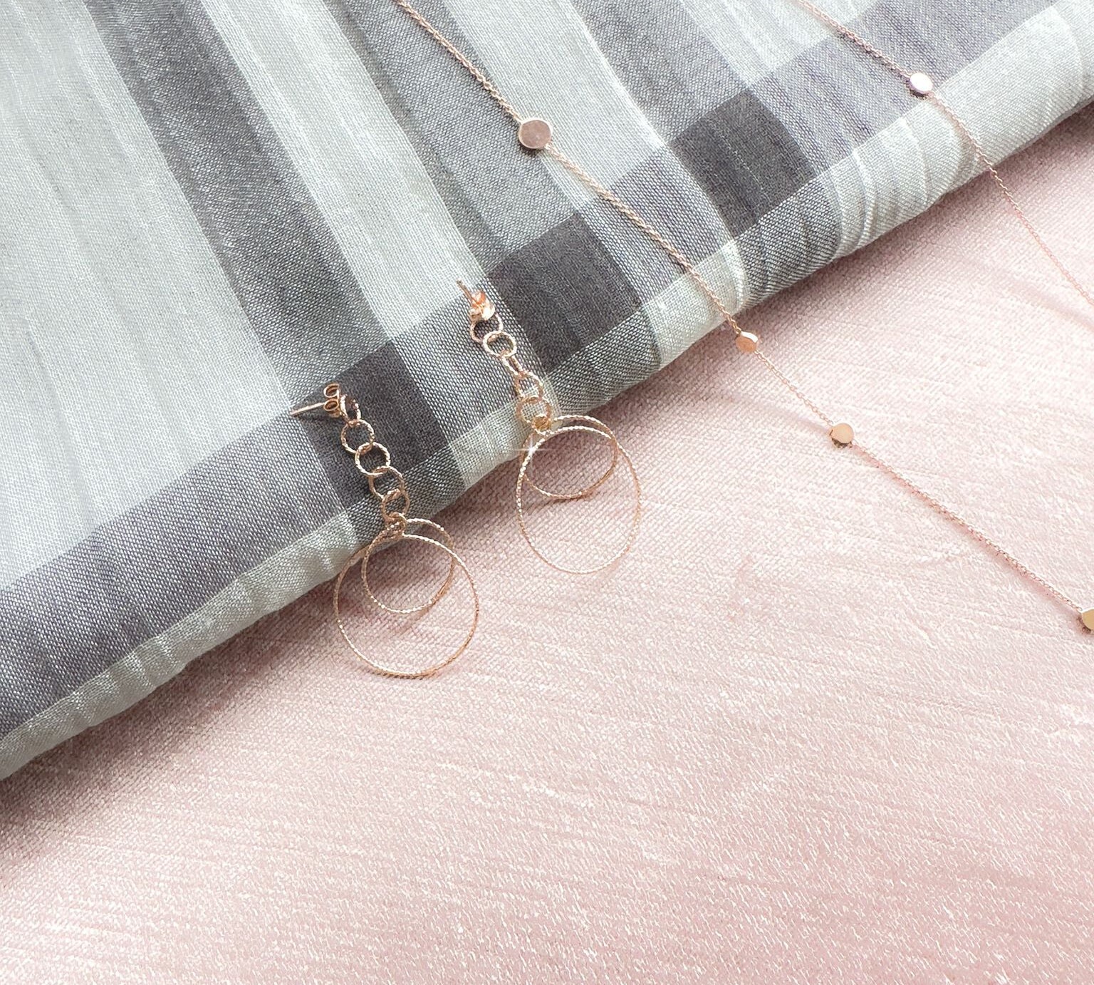 Close up view of Shimmering Chain Drop Earrings in rose gold, sparkling against a grey scarf. 