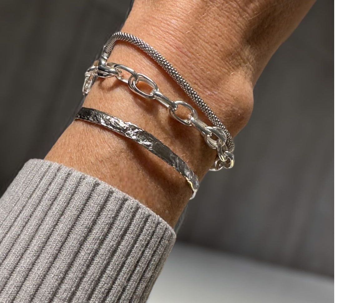 A closeup of the elegant Double Link Braclet worn on a wrist, along with two other silver bracelets.